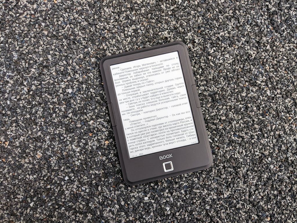 Digital BOOX e-book reader placed on a textured gravel surface, offering a tech contrast.